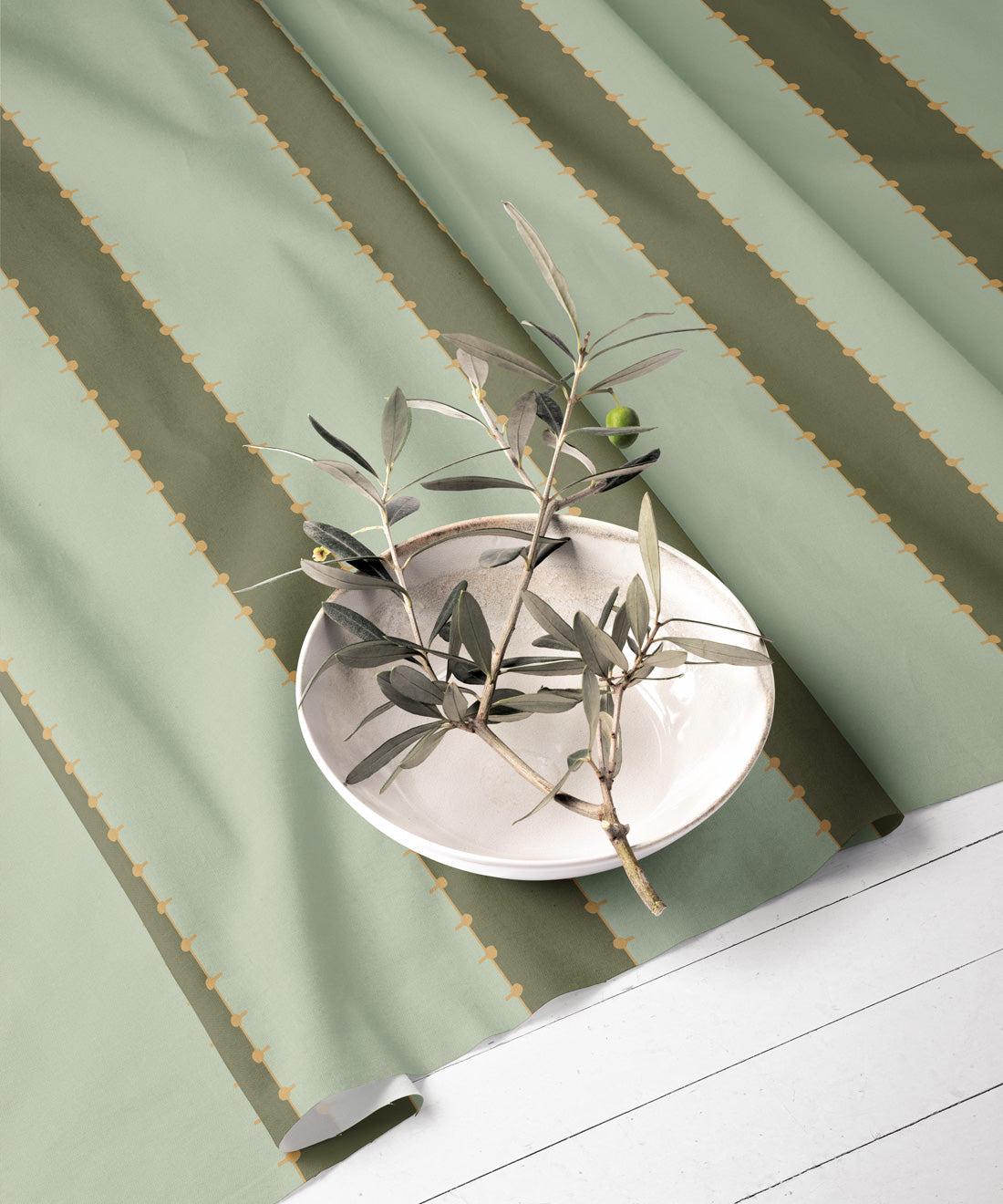 Green striped fabric with a decorative plate and olive branches on a white surface