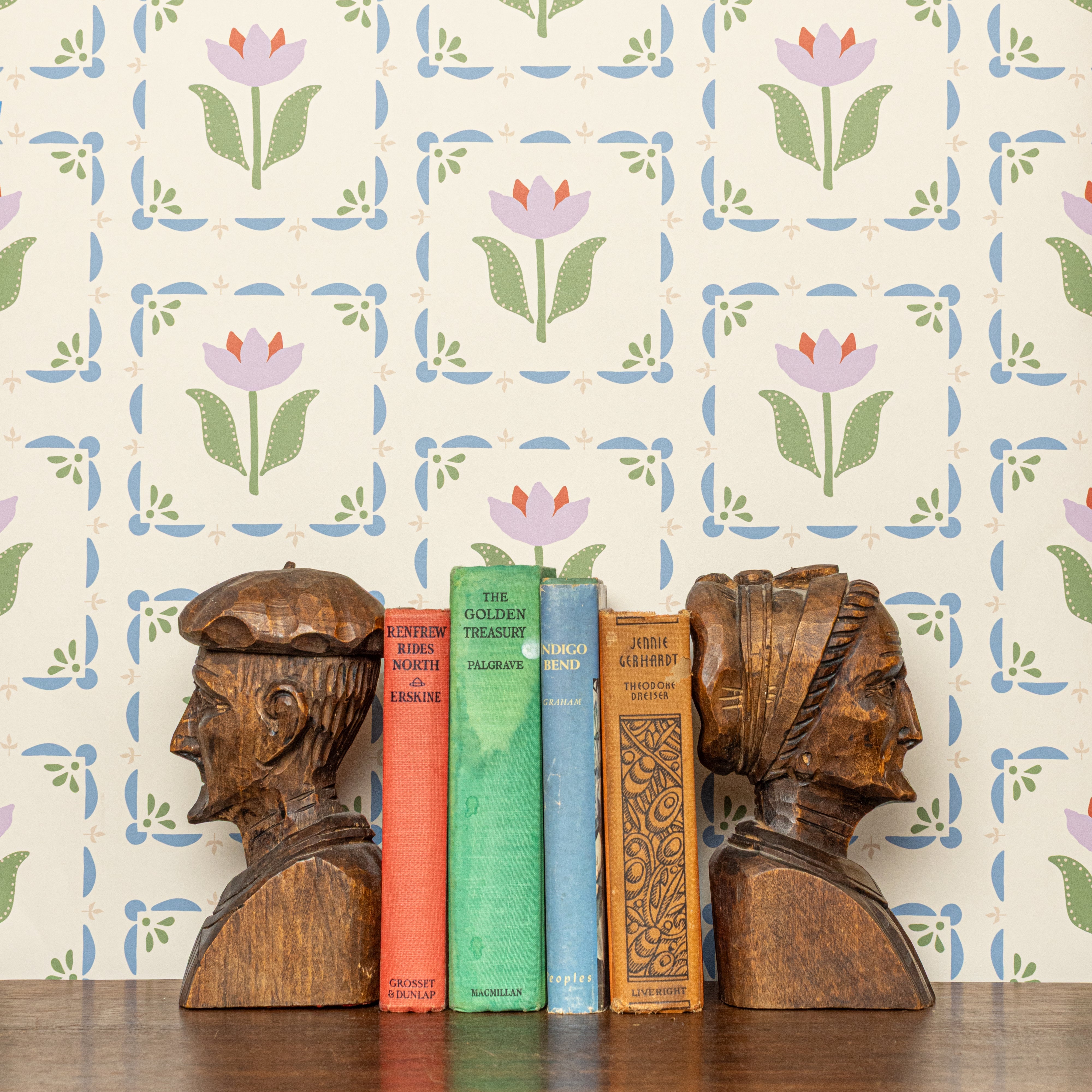 Wooden bookends shaped like human heads with books between them against a floral wallpaper background.