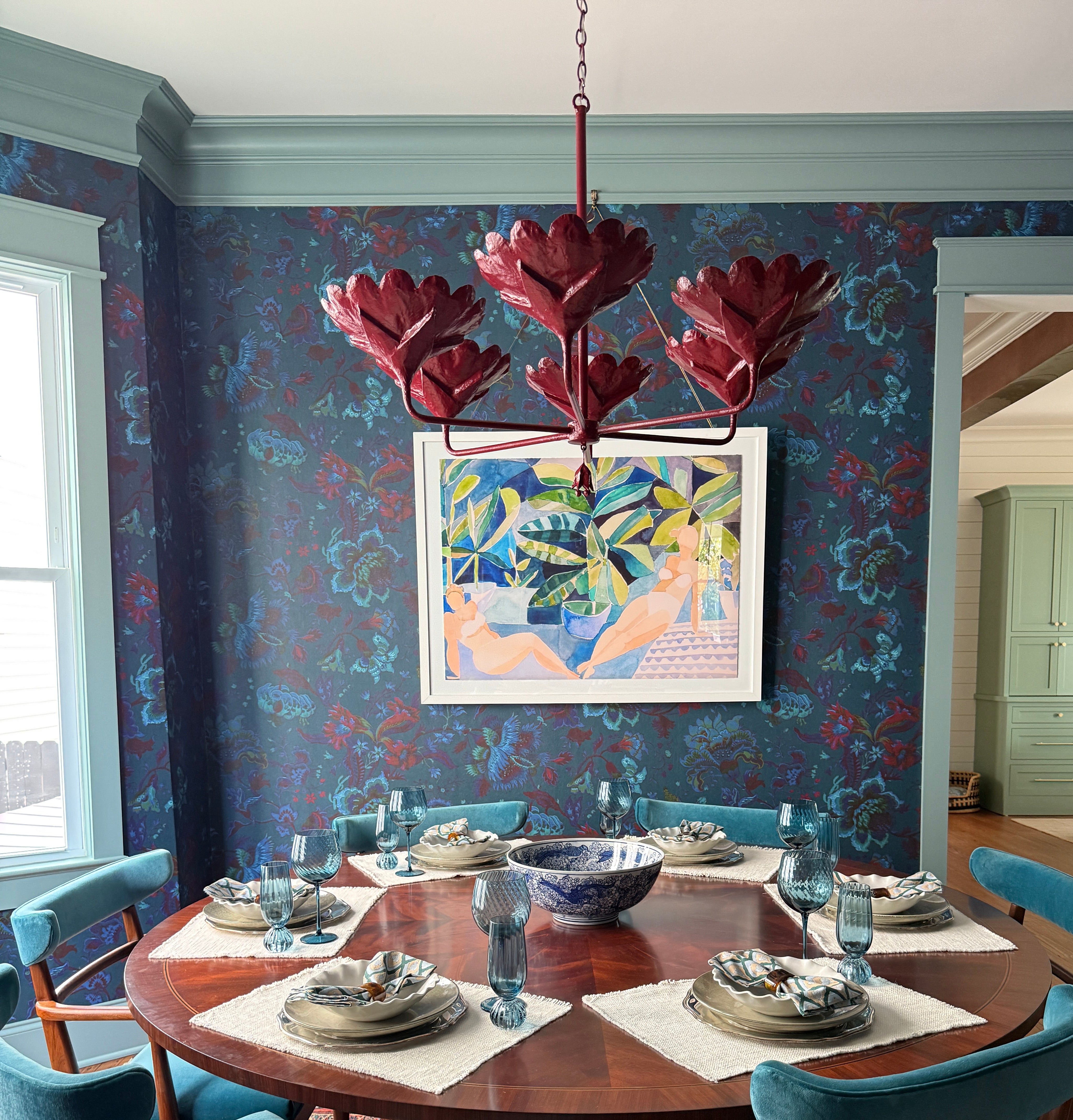 Dining room with a round wooden table, chairs, and a colorful wall painting.