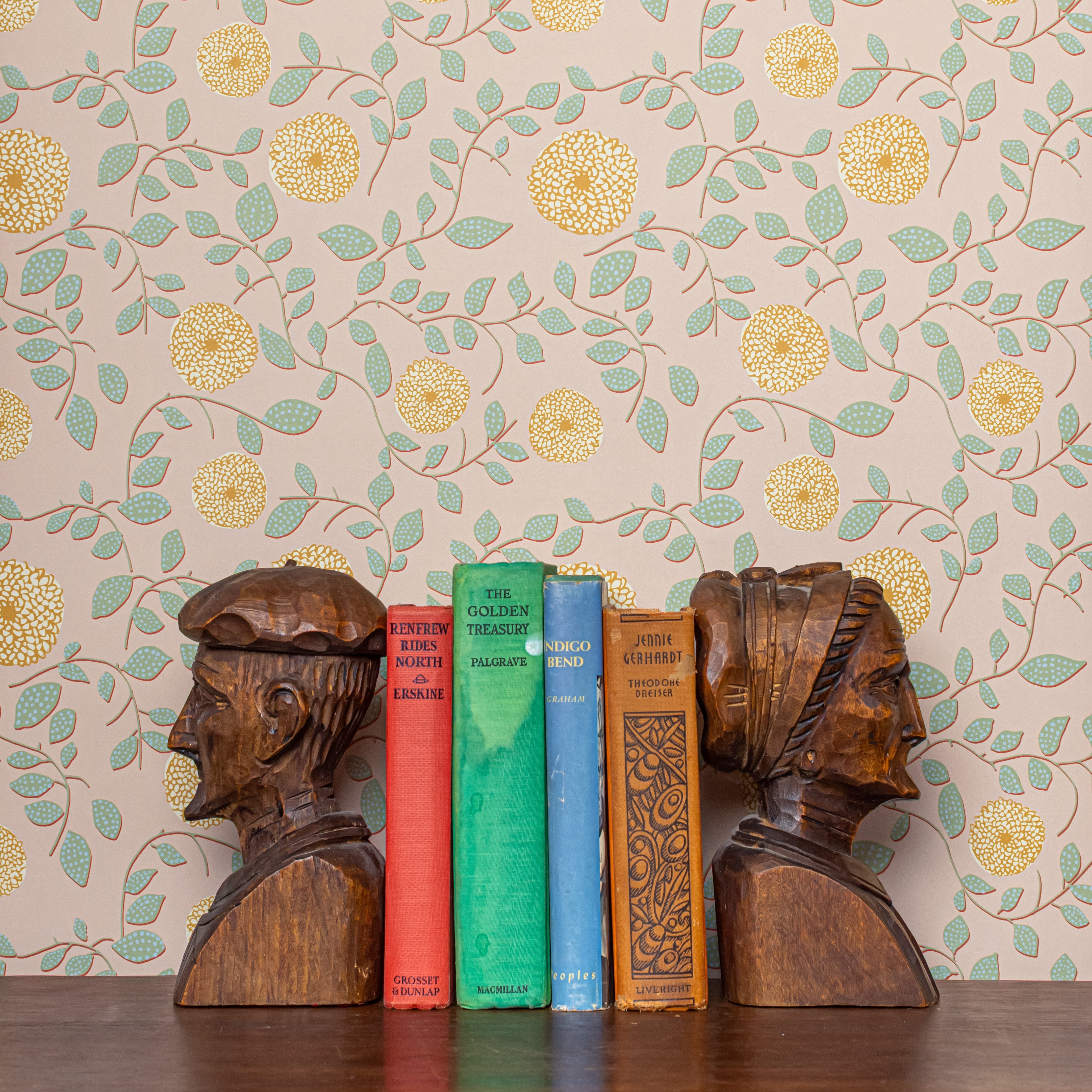 Wooden bookends shaped like heads with books on a floral wallpaper background
