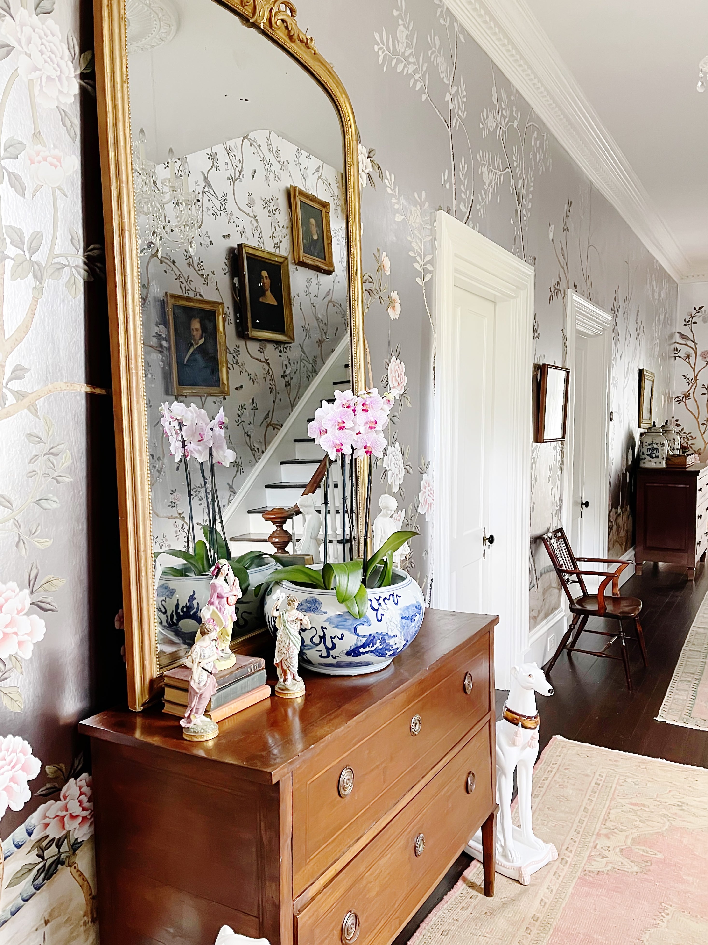 Decorative hallway with a large mirror, wooden dresser, and floral wallpaper.