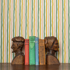 Wooden bookends shaped like human heads with a row of books against a chartreuse and green striped wallpaper background