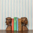 Wooden bookends shaped like human heads on a shelf with colorful books against a striped lavender and blue wallpaper background.