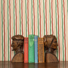 Wooden bookends shaped like faces on a row of books against a red and green striped wallpaper background