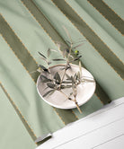 Green striped fabric with a decorative plate and olive branches on a white surface
