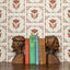 Wooden bookends shaped like faces with a row of books on a surface against a brown and black floral wallpaper background.