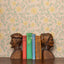 Wooden bookends shaped like human heads with books between them against a floral wallpaper background.