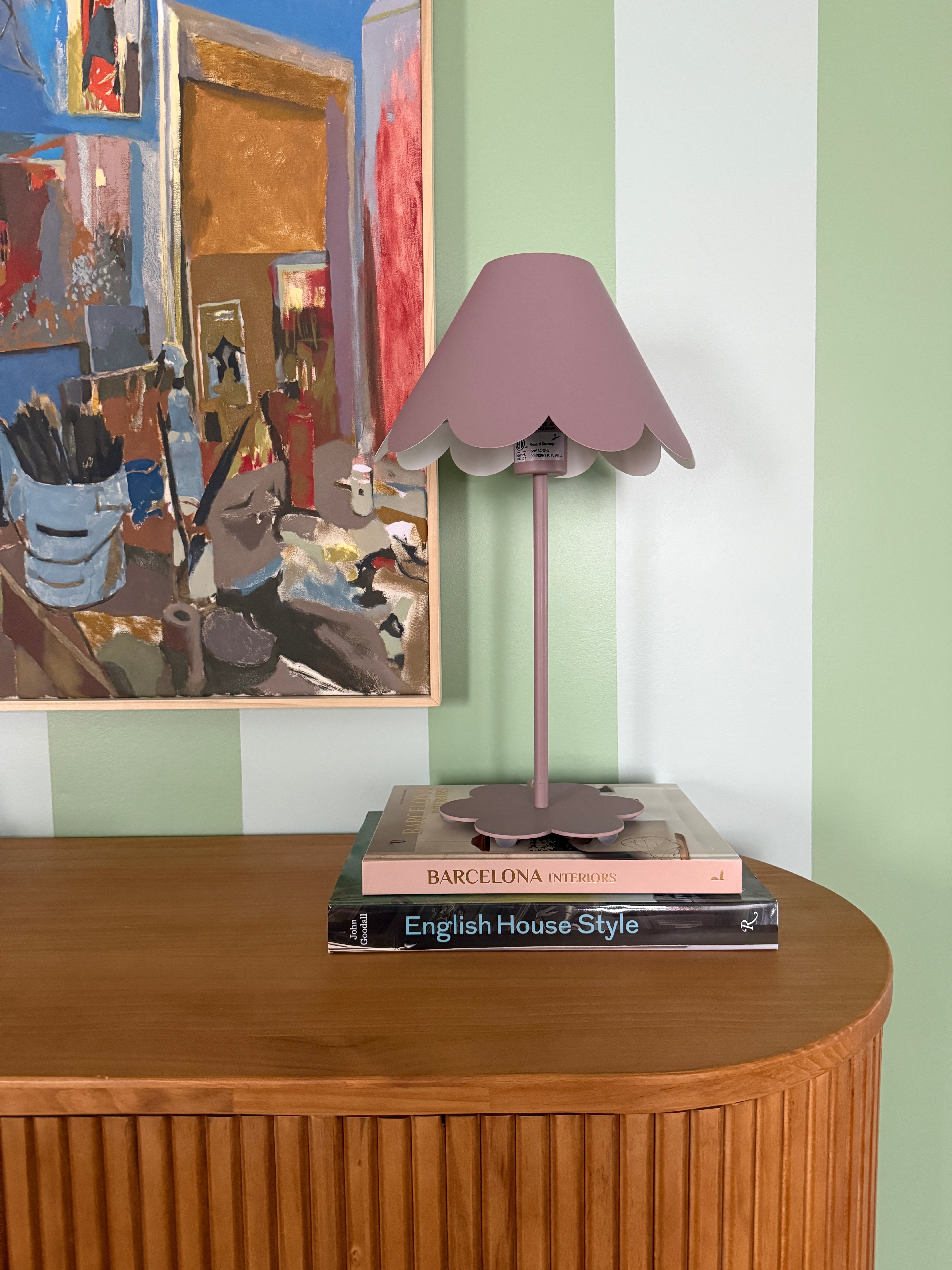 Decorative lamp with a book on a wooden surface against a striped wall.