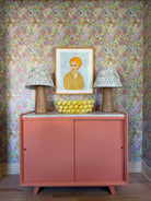 Pink entryway cabinet with a framed picture and floral-patterned wallpaper