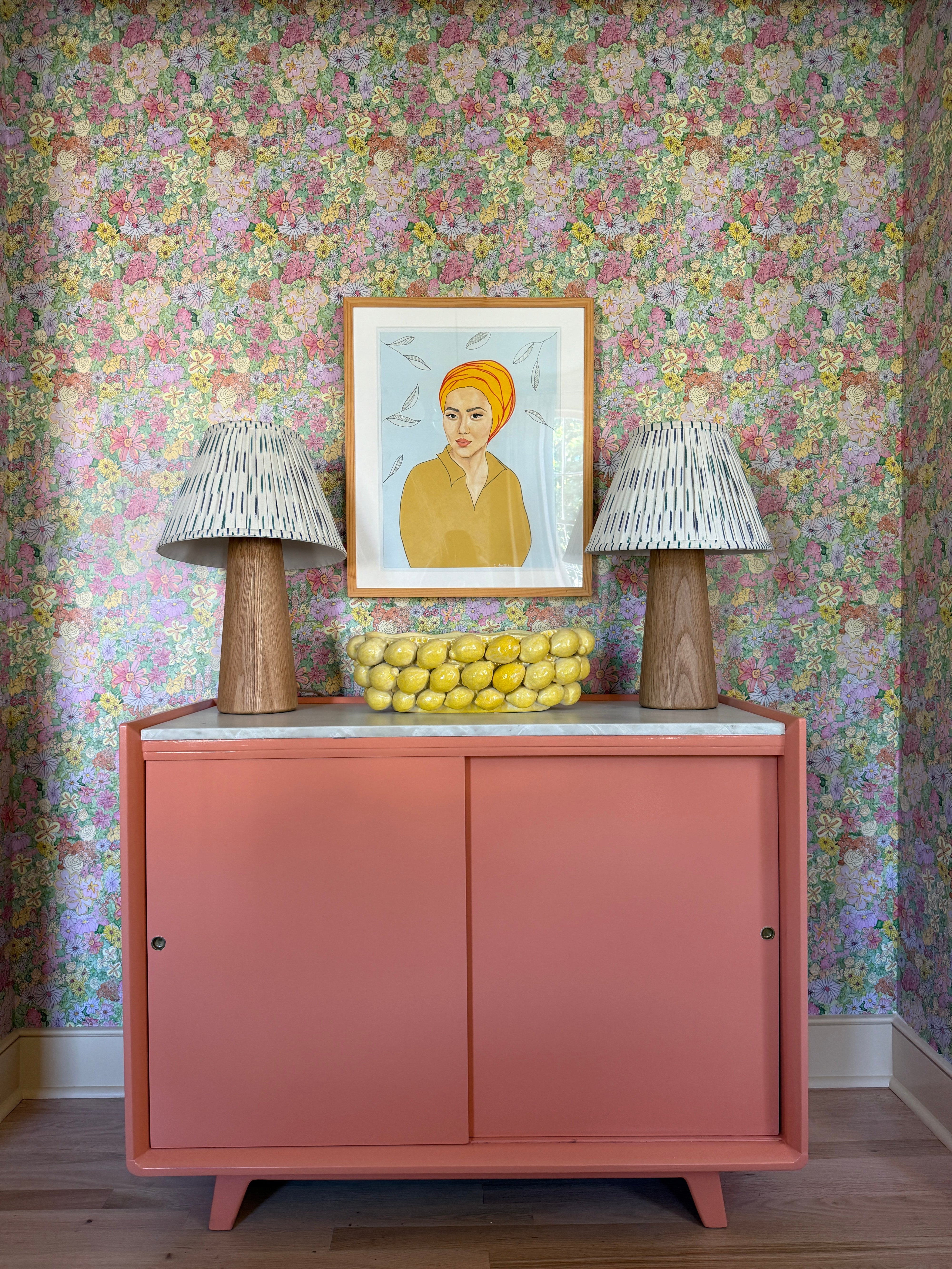 Pink entryway cabinet with a framed picture and floral-patterned wallpaper
